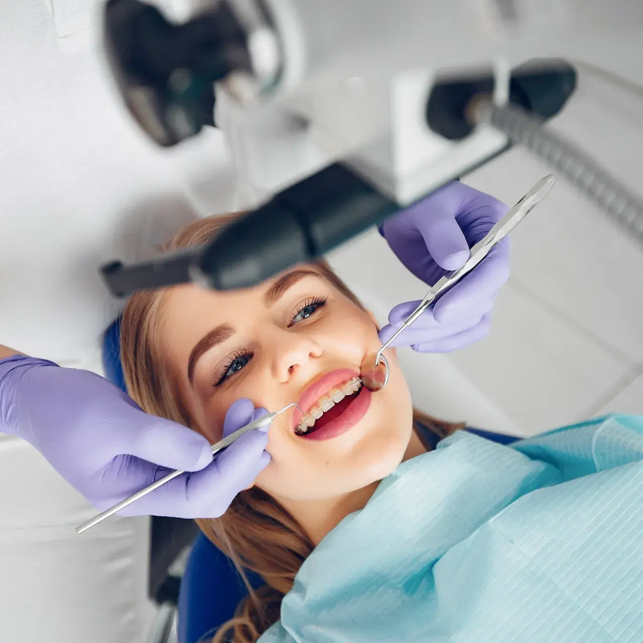 Giovane paziente con apparecchio ortodontico durante una visita di controllo odontoiatrico, assistita da un dentista con guanti viola e strumenti dentistici